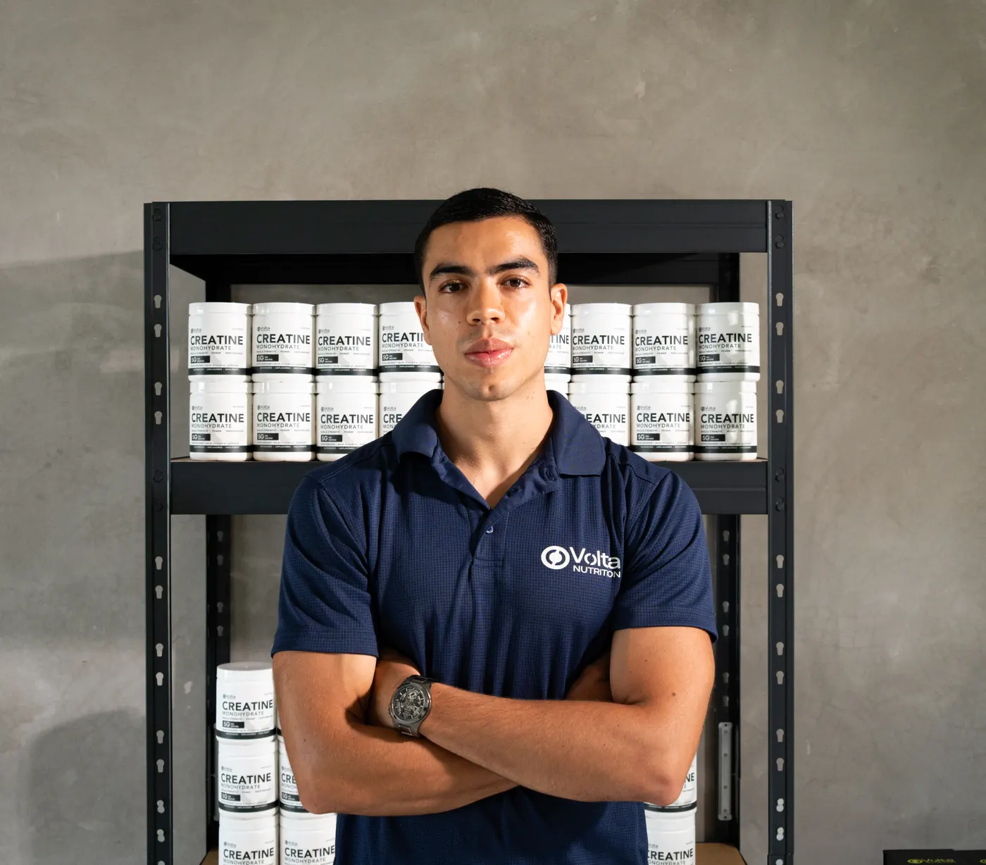 Alejandro Díaz, fundador de Volta Nutrition, con los brazos cruzados frente a una estantería con botes de Volta Creatine