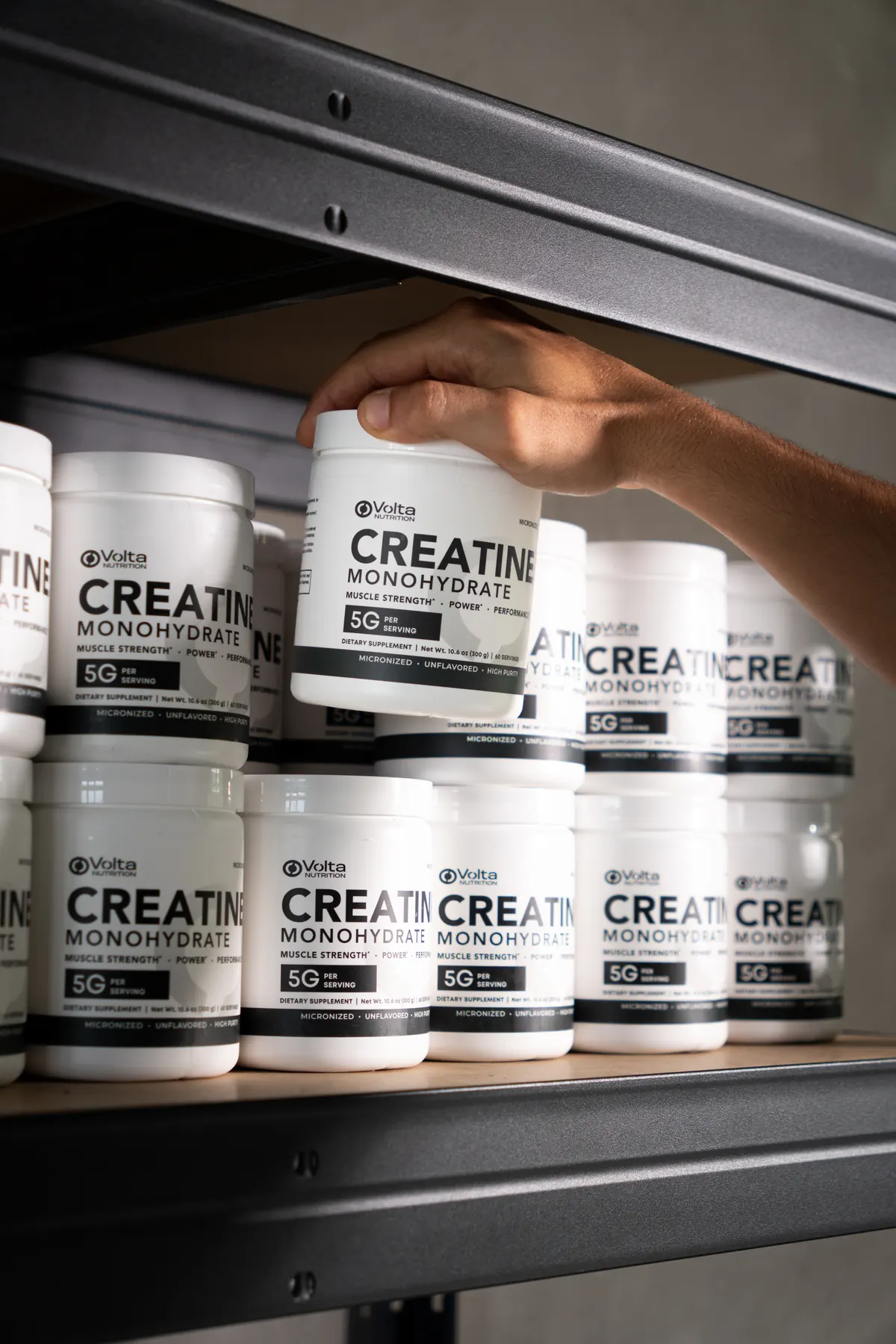 Una mano toma un bote de Volta Creatine de una estantería llena de botes